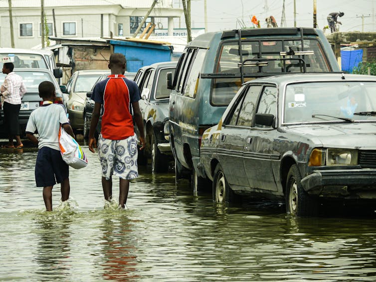 People walk past cars on flooded street