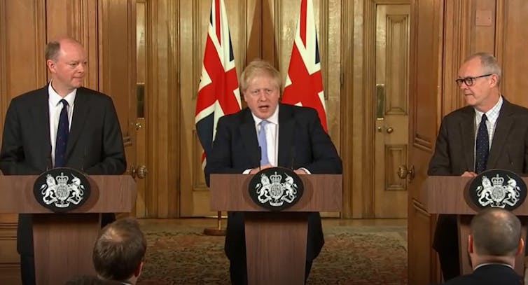 Prime Minister Boris Johnson, Chief Medical Officer Chris Whitty and Chief Scientific Adviser Sir Patrick Vallance speaking at lecterns in front of union flags.