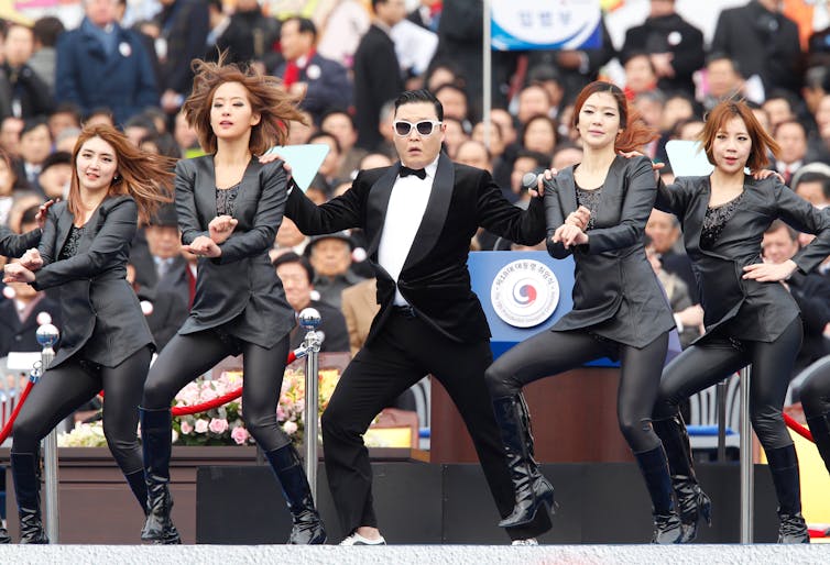 A man dressed in a tuxedo is on stage surrounded by backup dancers.