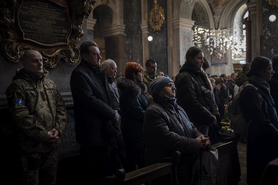 A group of people stand with solemn looks on their faces in a dimly lit church