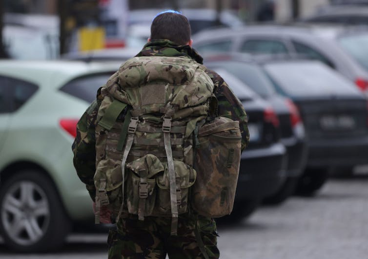 Man in military fatigues walks through parking lot.