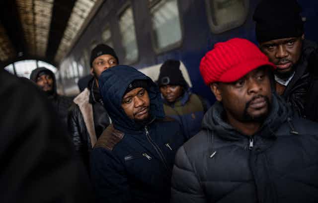 7 African refugees dressed in warm jackets and caps wait for a train at a train station