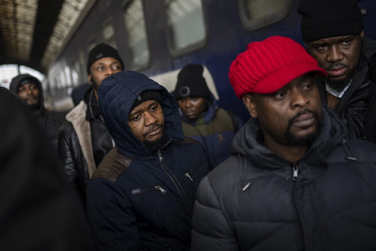 7 African refugees dressed in warm jackets and caps wait for a train at a train station