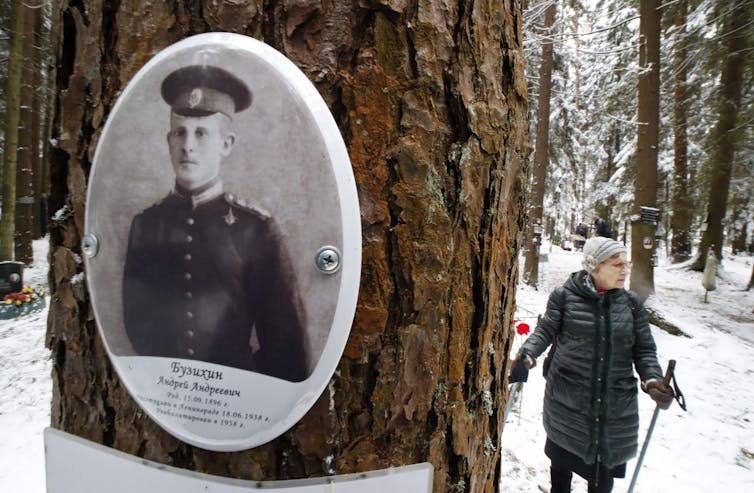 A portrait of a victim of the Great Terror is in the foreground on a tree while a woman walks in the snow in the background