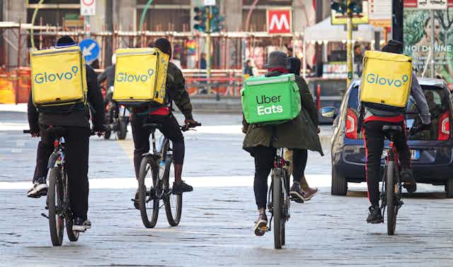 Four people biking down the street with branded coolers on their backs