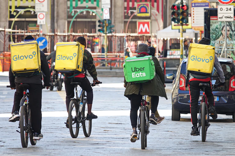 Four people biking down the street with branded coolers on their backs