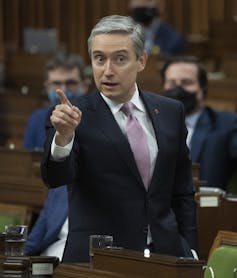 A man in a suit standing up and giving a speech