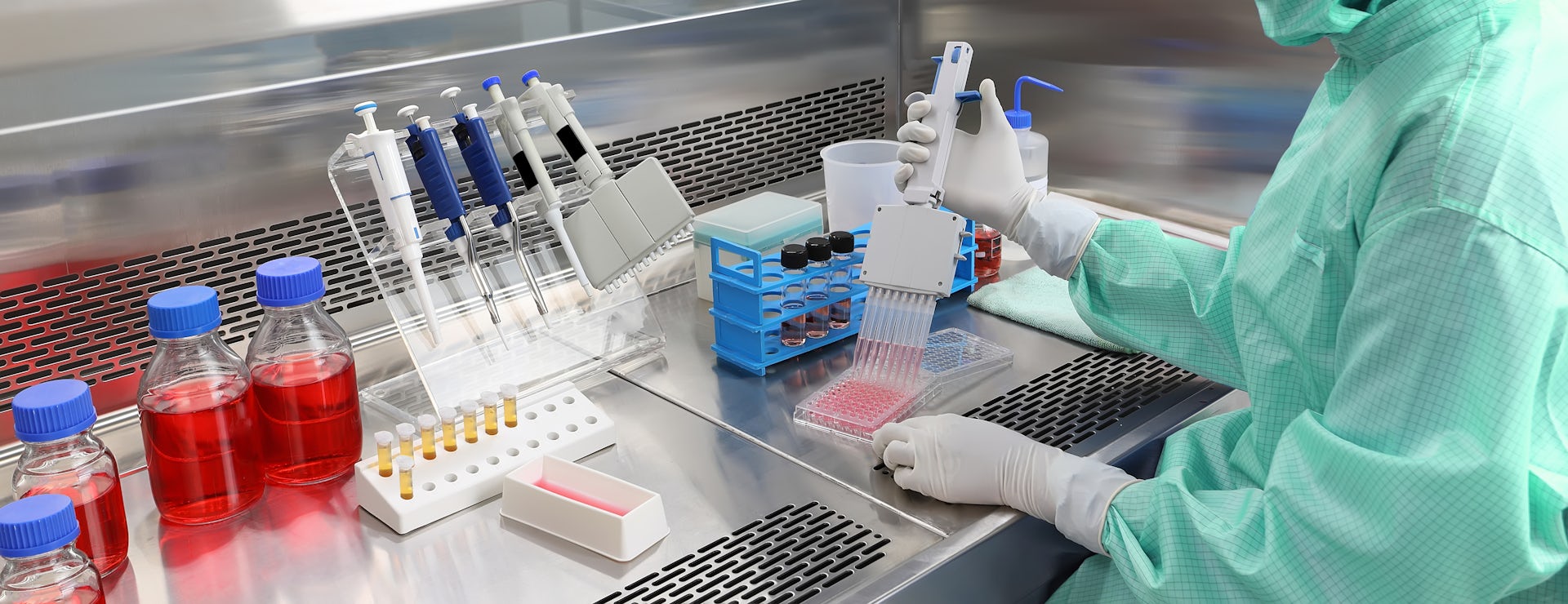 A person wearing PPE using a multi-channel pipette in a laboratory