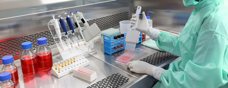 A person wearing PPE using a multi-channel pipette in a laboratory