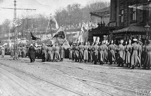 A black and white photo depicts Ukrainian soldiers marching while holding aloft flags.