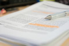 A stack of journal articles, with passages highlighted in the top one, with a pen resting on them.