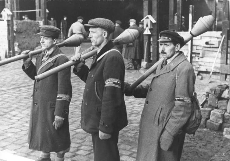men in a black and white photo hold anti-tank weapons over their shoulders