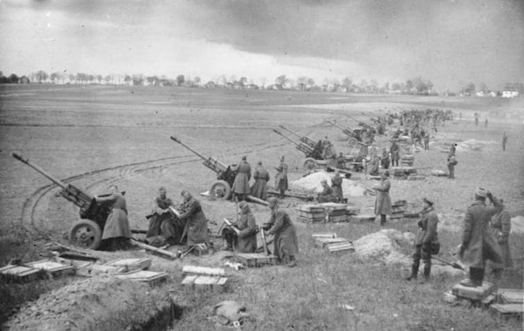 a line of artillery guns point across a field in a black and white photo.