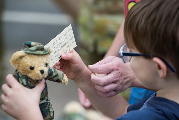 Child holds a bear wearing an army camouflage uniform