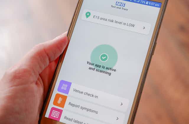 A person holding a phone running the NHS contact-tracing app