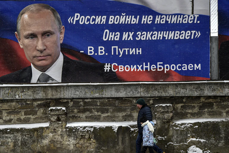 A man walks past a poster of the Russian president Vladimir Putin, on a wall in Crimea.