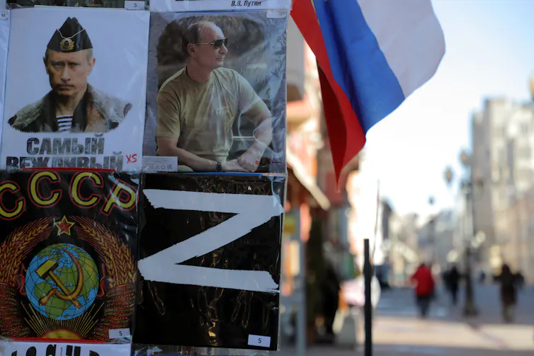 A Russian flag and pictures of Putin and a large Z on a board outside a shop.