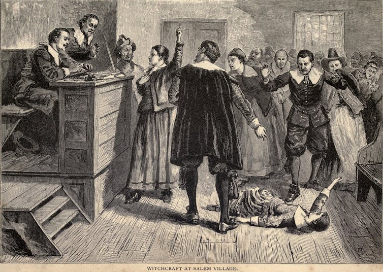 A young girl convulses on the floor of a court room as a woman stands before a judge accused of witchcraft.