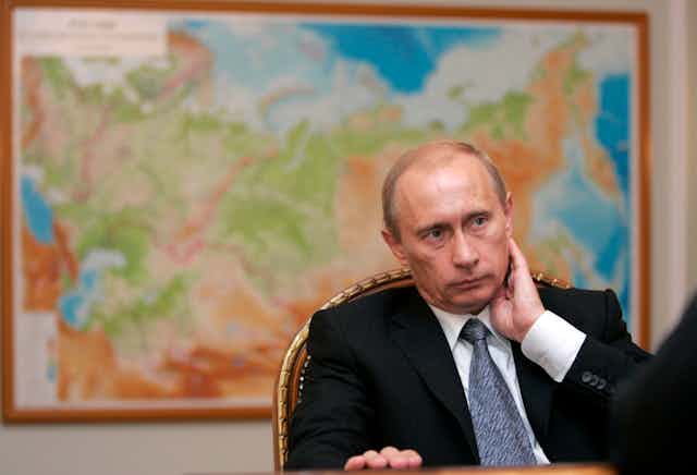 Vladimir Putin sitting in front of a map of Russia