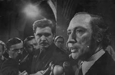 A black and white photo of a man speaking to reporters.