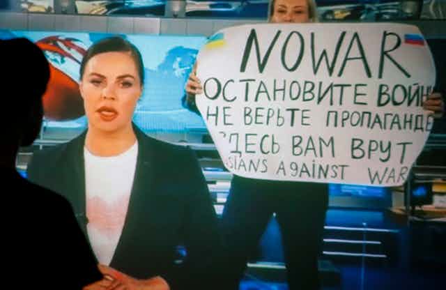 Screenshot of Russia's Channel 1 network news bulletin with journalist Marina Ovsyannikova holding up an anti-war message in the background.