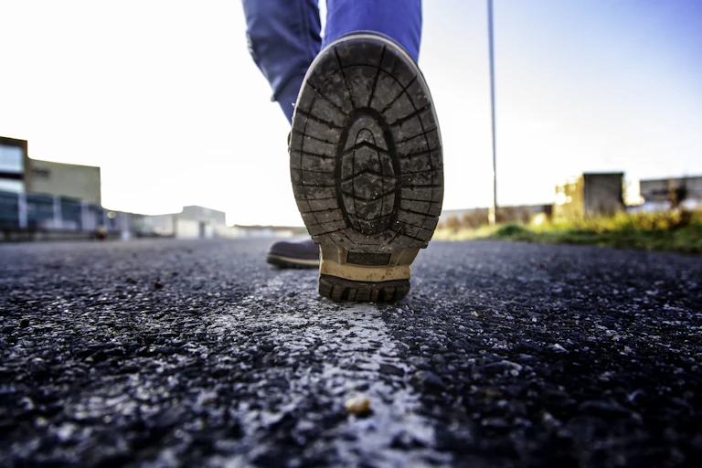 Vue ras du sol d'un homme en train de marcher, gros plan sur la semelle de son pied gauche