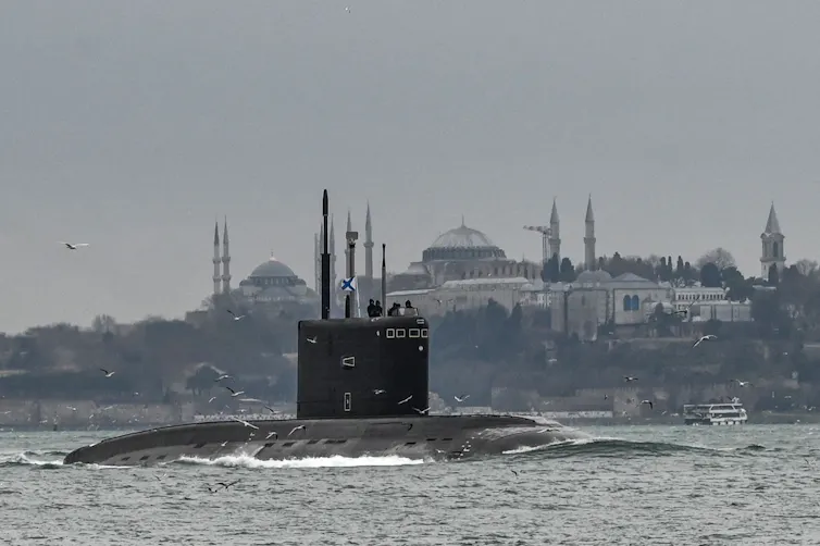A black submarine is seen sailing before it submerges underneath the sea.