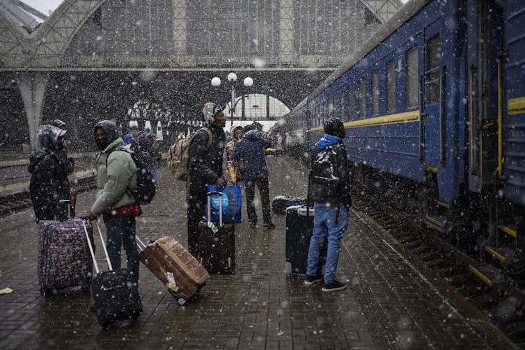 A group of Black students wait at a railway station with suitcases.