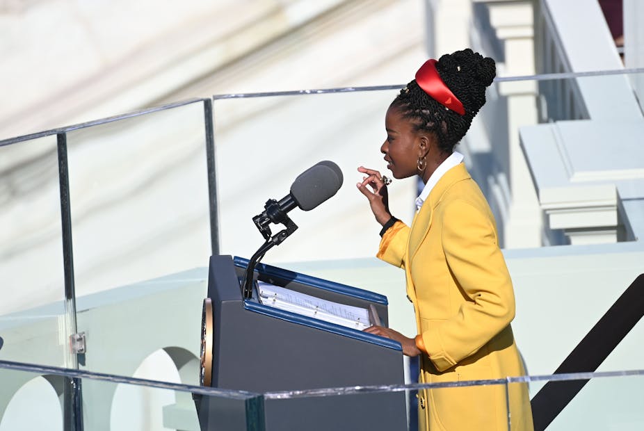 A young Black girl stands at a lectern to recite a poem on stage.