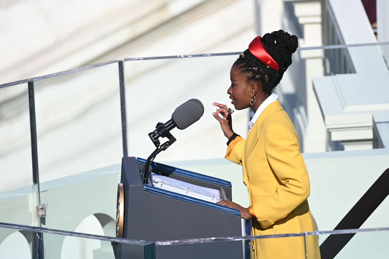 A young Black girl stands at a lectern to recite a poem on stage.