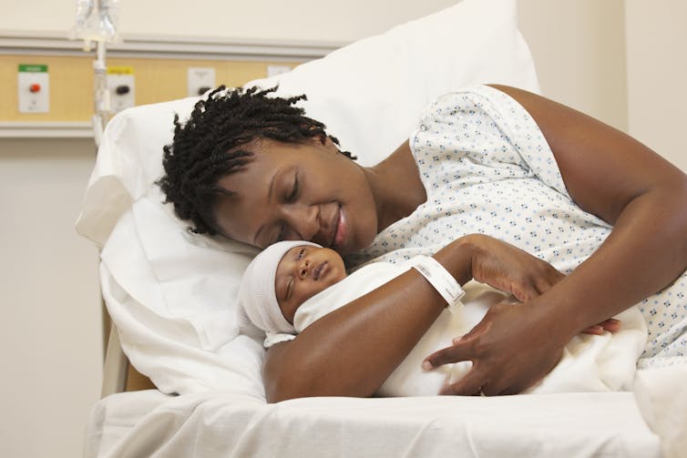 A woman in a hospital bed holds her newborn baby.