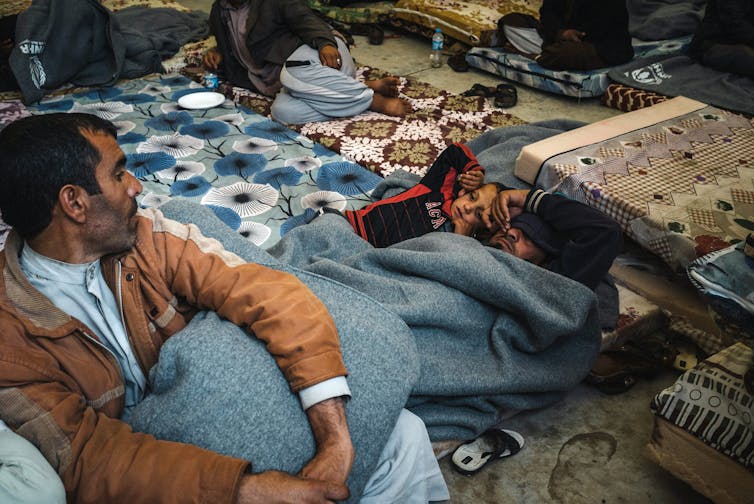A man and children lie under blue-grey blankets.