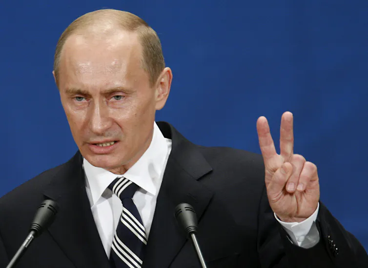 An angry man standing in front of two microphones raises two fingers