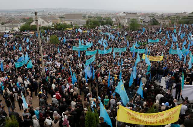 A rally with large number of people holding yellow banners and blue flags.