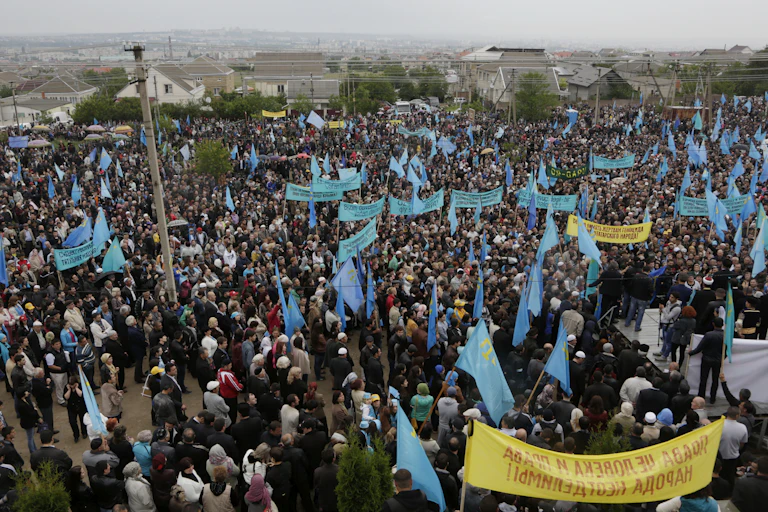 A rally with large number of people holding yellow banners and blue flags.