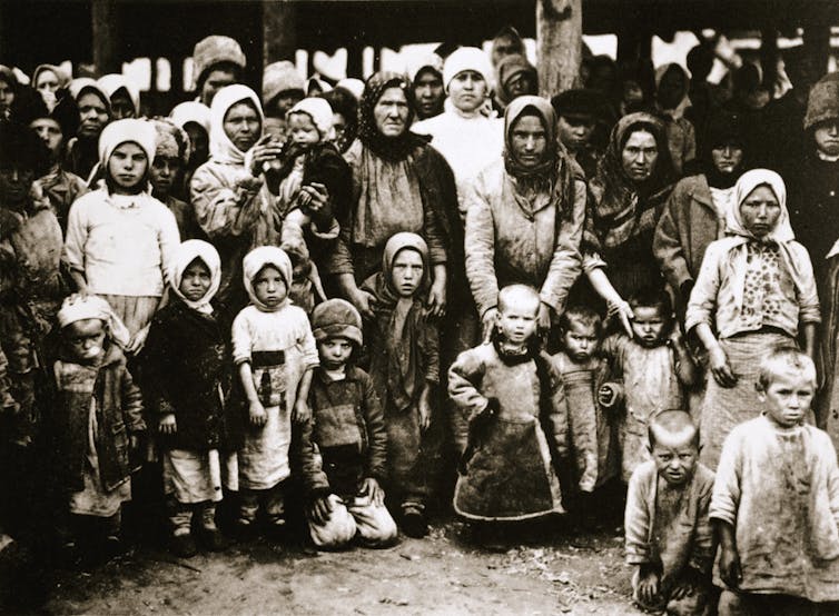 A group of starving peasant women and children, many of them with scarves wrapped around their heads.