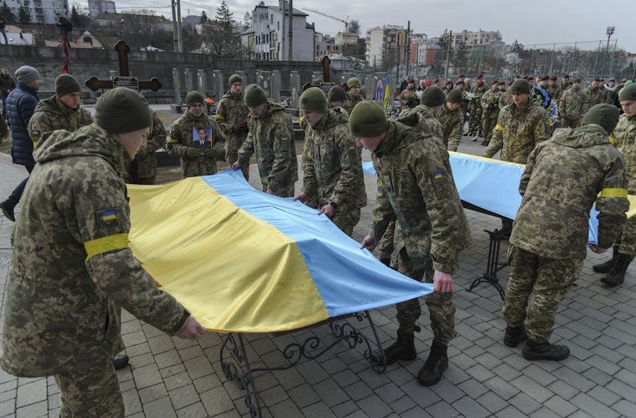 Soldiers laying Ukrainian flags over coffins. 