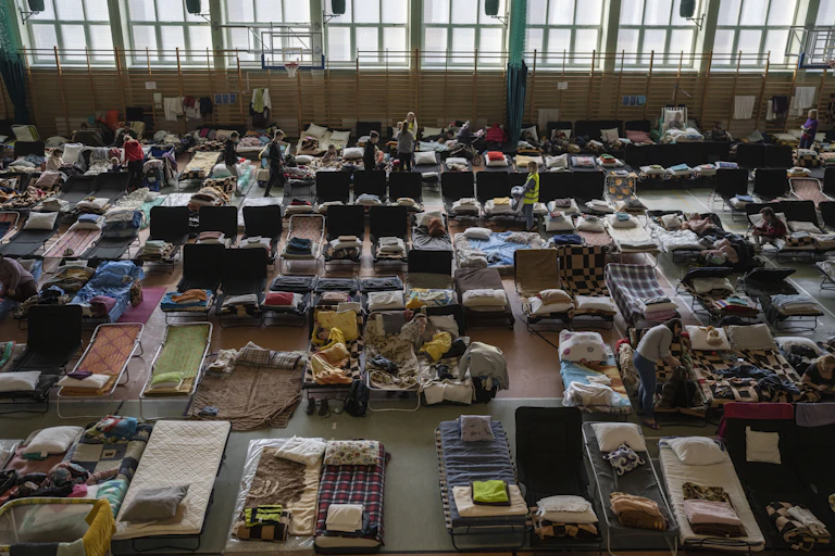 Cots and people are seen in a gymnasium