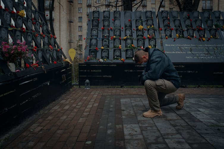 A man kneels in front of a memorial.