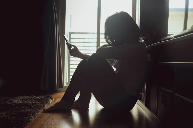 Person sitting on ground looking at phone in dark room