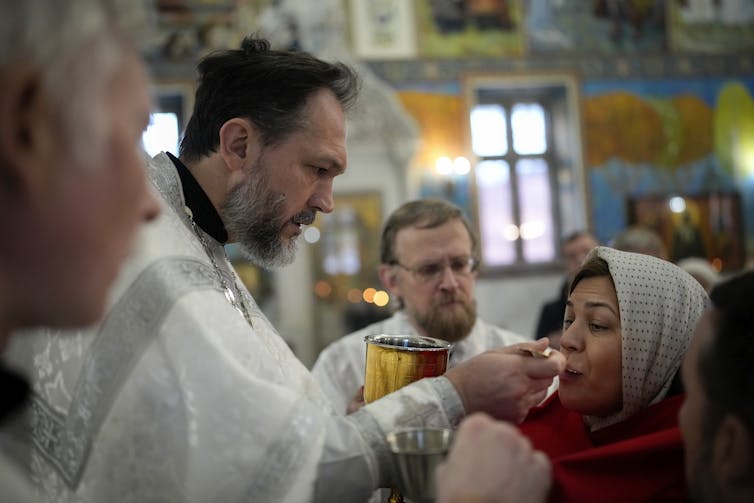 A priest offers Communion to a woman wearing a kerchief.