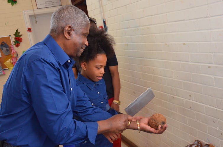 An older man shows a child how to crack a coconut.