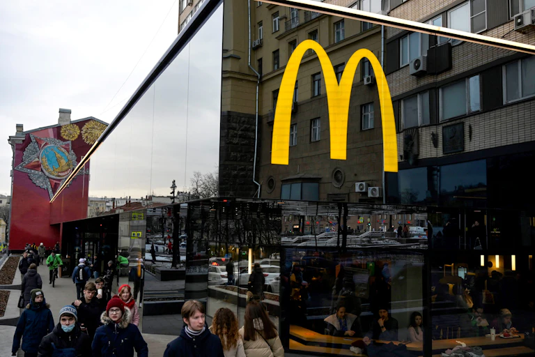 People in winter clothes walking past a McDonalds restaurant with big golden arches on it.