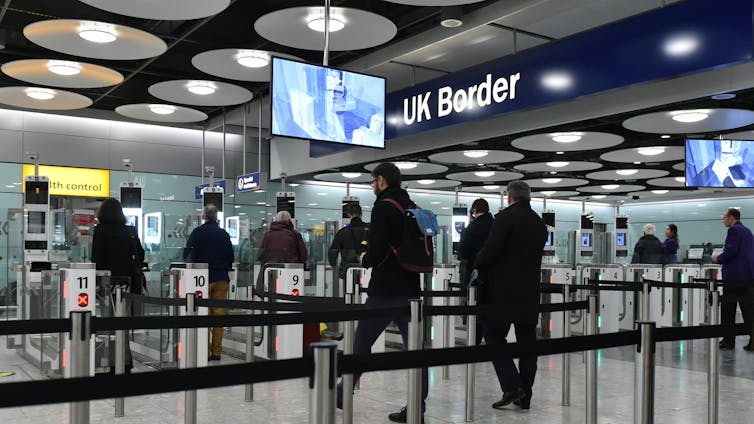 People approaching electronic gates at an airport, under a blue sign reading UK Border