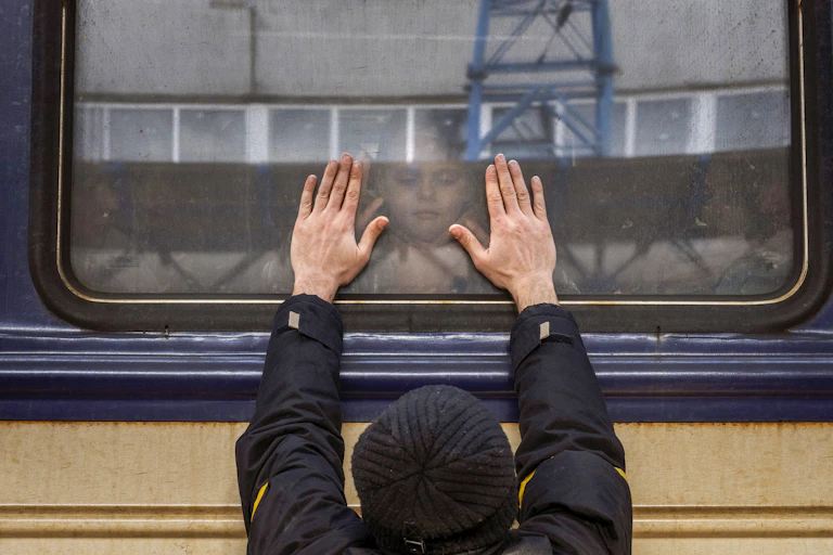 A man presses his palms against a train window as his daughter looks down at him through the glass.
