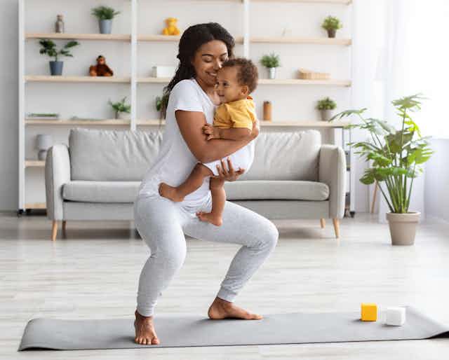 Woman holding a baby doing squats on a mat at home