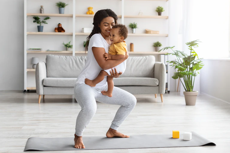 Woman holding a baby doing squats on a mat at home