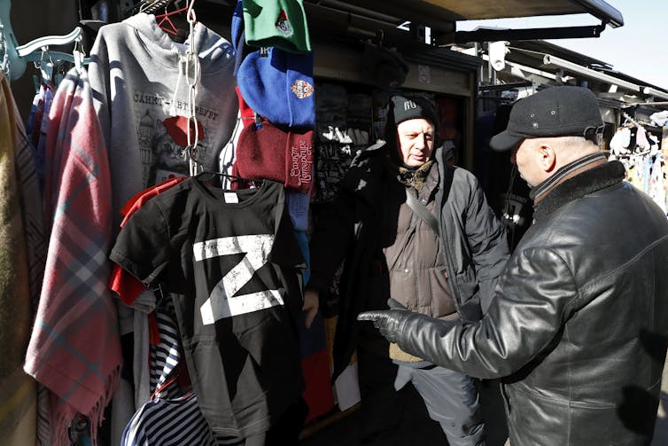 A man points at a black t-shirt with a letter Z on it at a souvenir stall