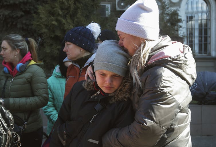 A crying woman and child wearing warm hats and coats embrace.