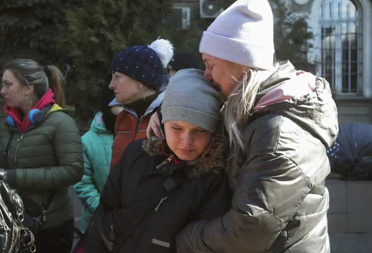 A crying woman and child wearing warm hats and coats embrace.